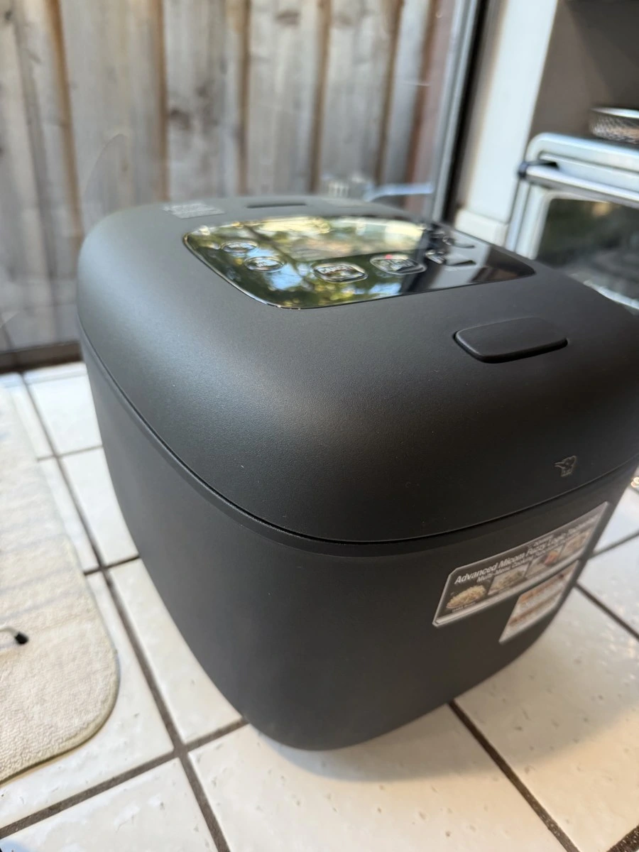 Close-up photo of the matte-rough zaratsuita black exterior finish, top lid-release button, and elephant logo on my Zojirushi NL-EAC18BA
