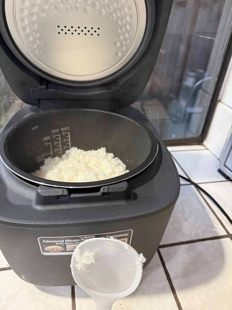 Inside of my Zojirushi NL-EAC18 B683 black nonstick inner pot showing high-contrast white water level marks for Congee, Sushi, White, and Steel Cut Oatmeal with cooked white rice
